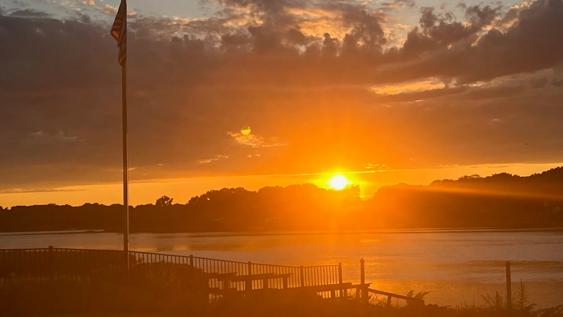 El atardecer ilumina un cuerpo de agua tranquilo, con una barandilla en primer plano.