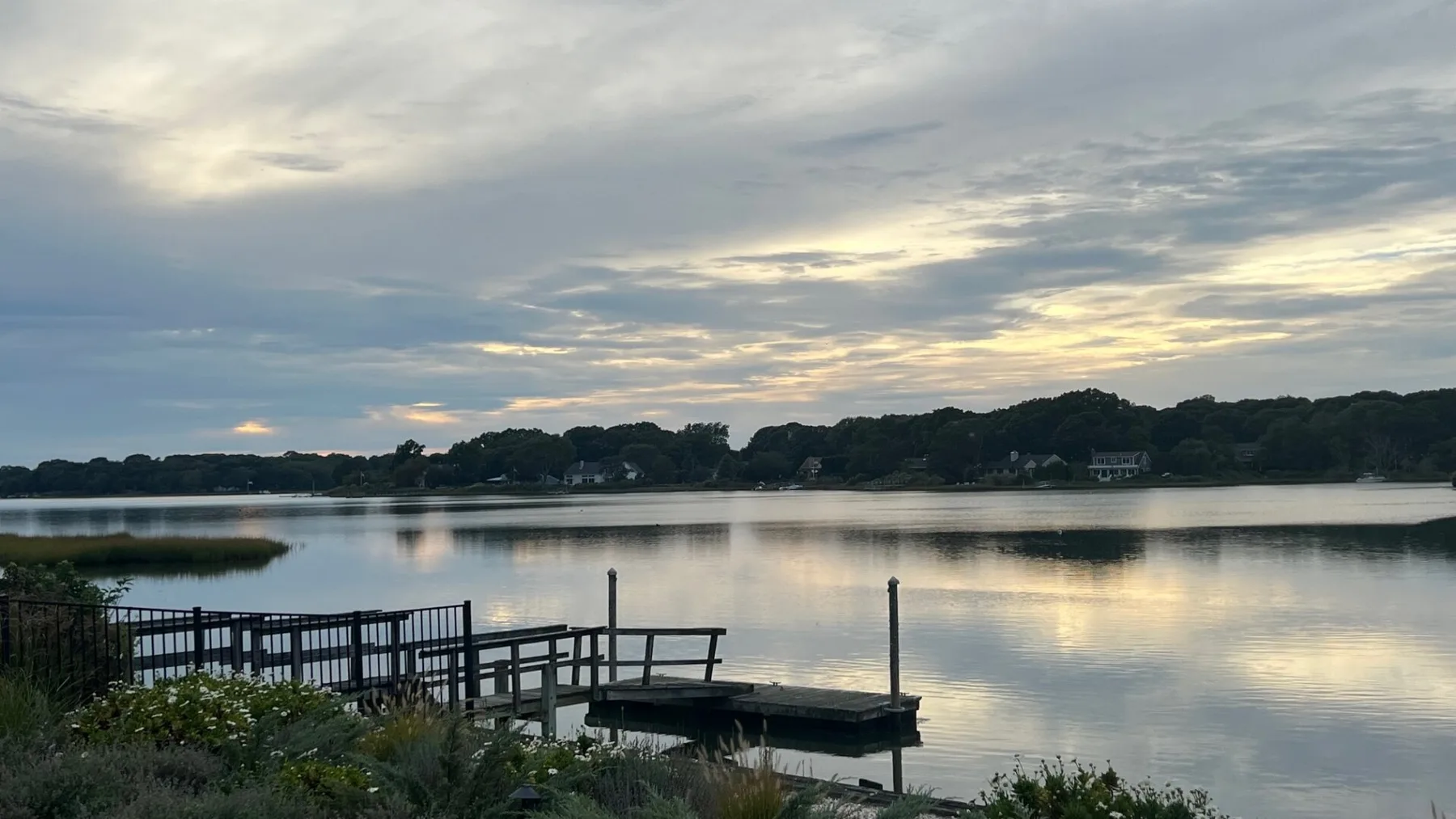 A lakeside scene at dusk with a wooden dock extending over calm water.