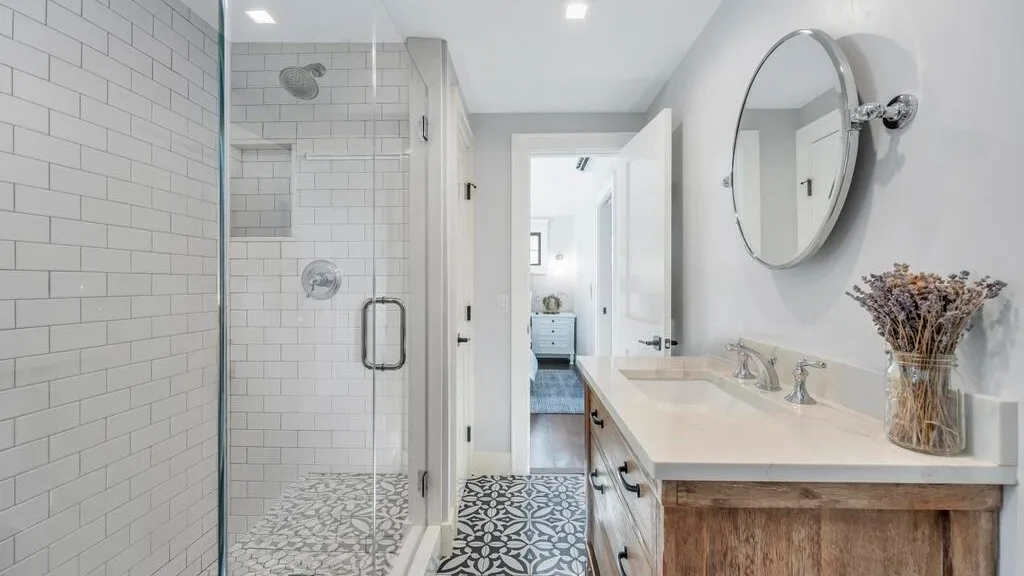 Un baño luminoso con ducha de azulejos y un lavabo largo.