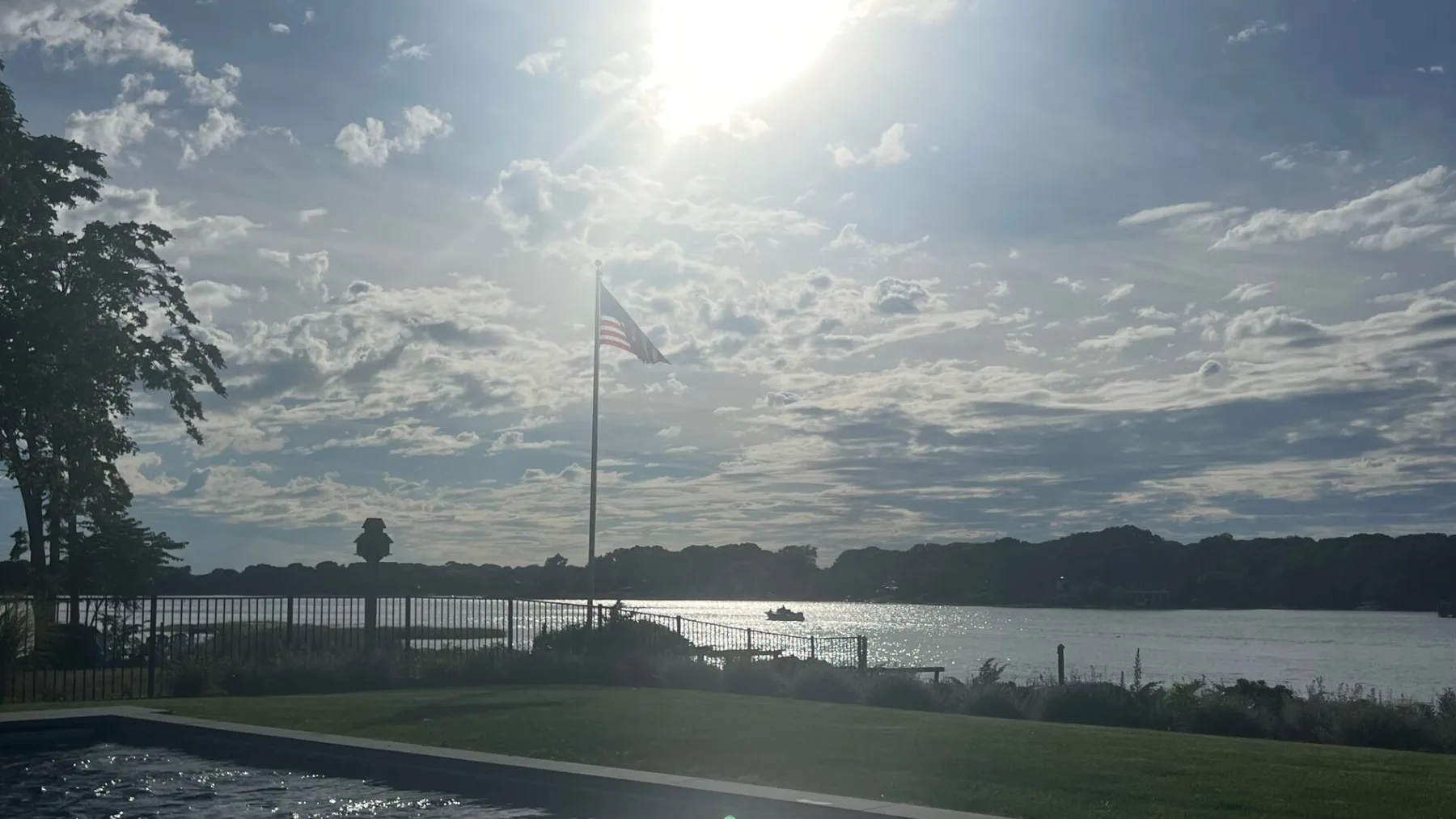 Vista junto al lago con una bandera estadounidense junto al agua bajo un cielo parcialmente nublado.