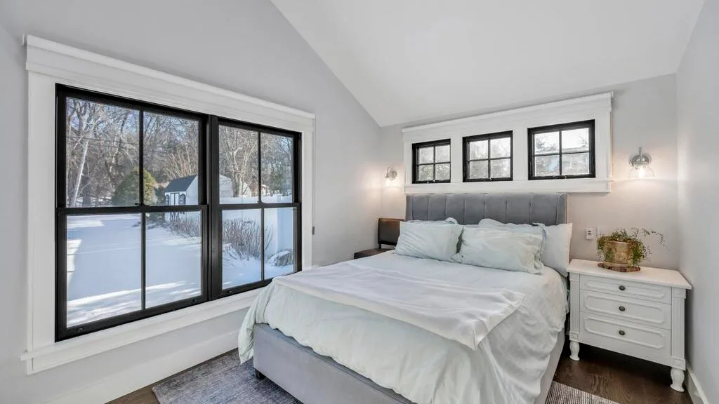 Un dormitorio luminoso tiene una cama bajo tres ventanas, con nieve visible afuera.
