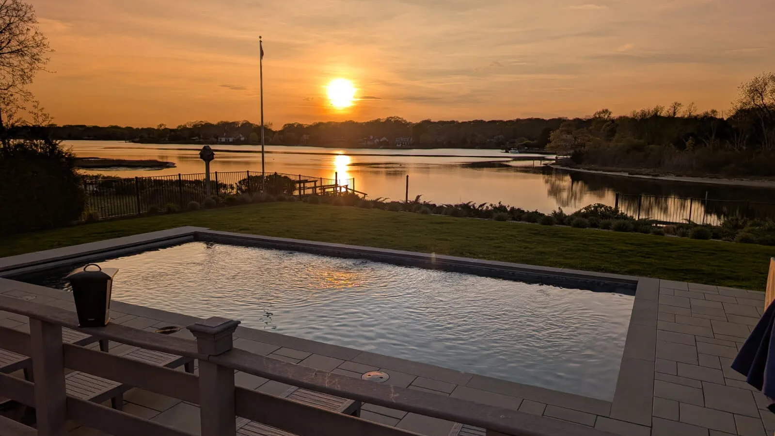 A swimming pool overlooks a calm lake at sunset.