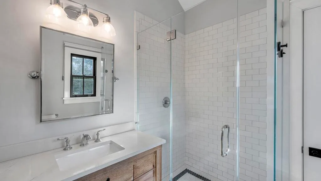 Un baño luminoso con lavabo, espejo y ducha con mampara de vidrio.