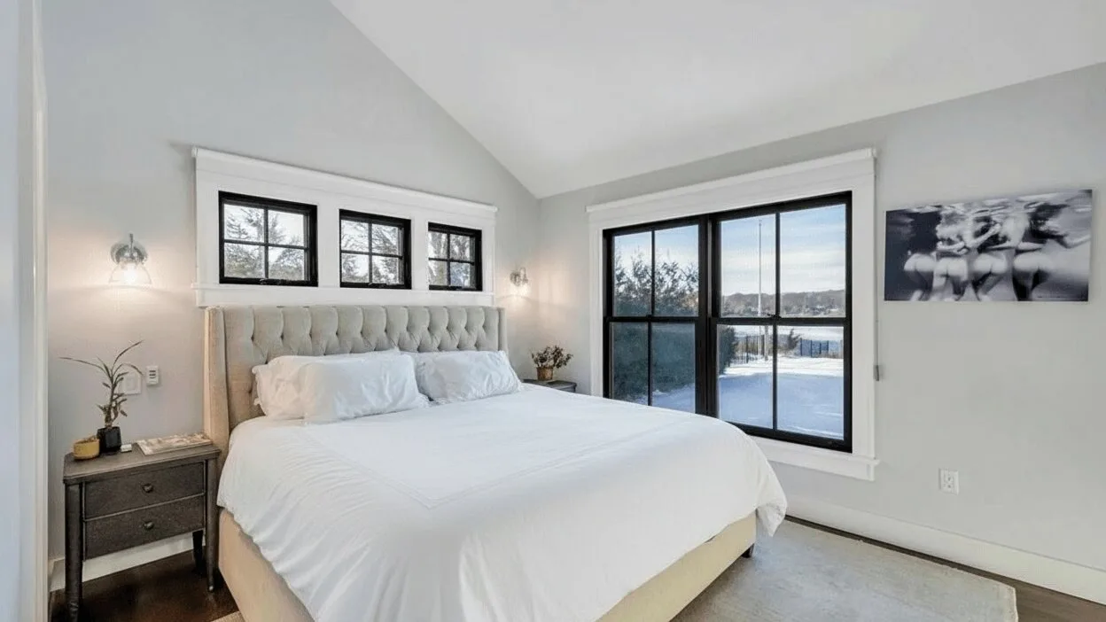Un dormitorio luminoso con una cama bien tendida y grandes ventanas con vista a la nieve.