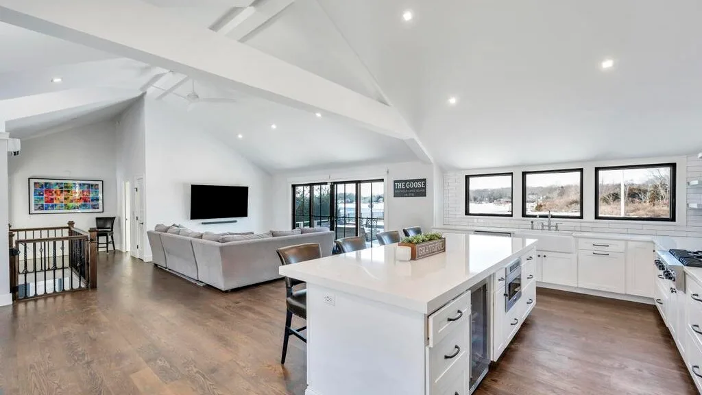 Sala de estar y cocina de concepto abierto, con gabinetes blancos y amplias ventanas.