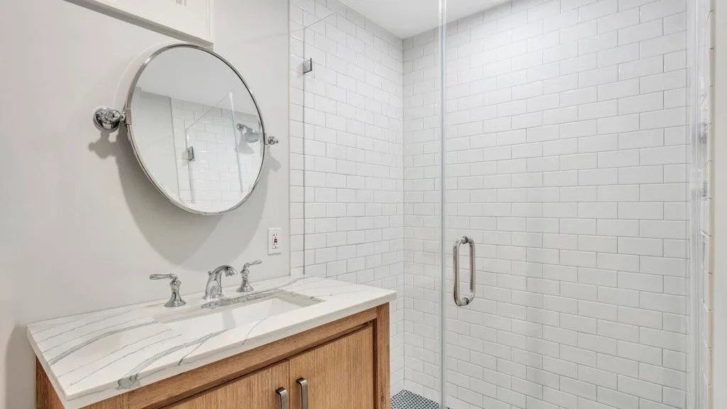 Un lavabo de baño con espejo redondo junto a una ducha revestida de azulejos.