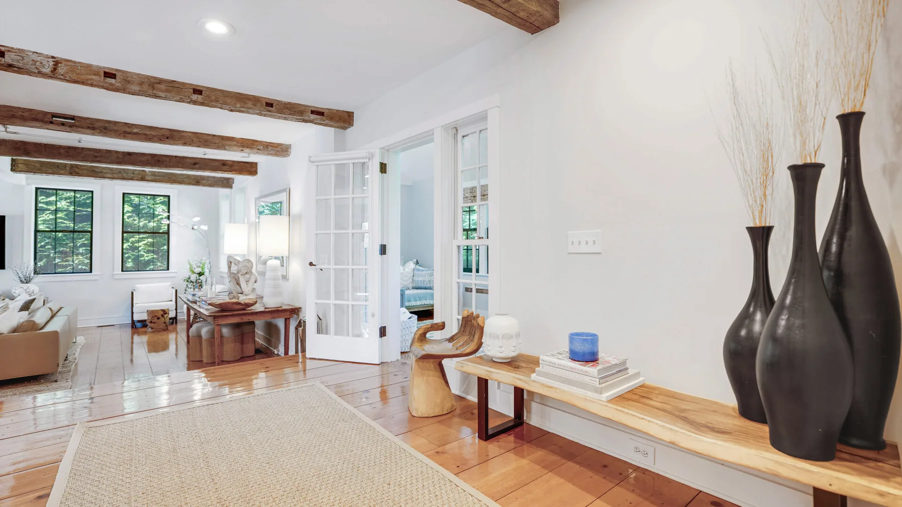 A bright living room with exposed ceiling beams and a large woven rug.