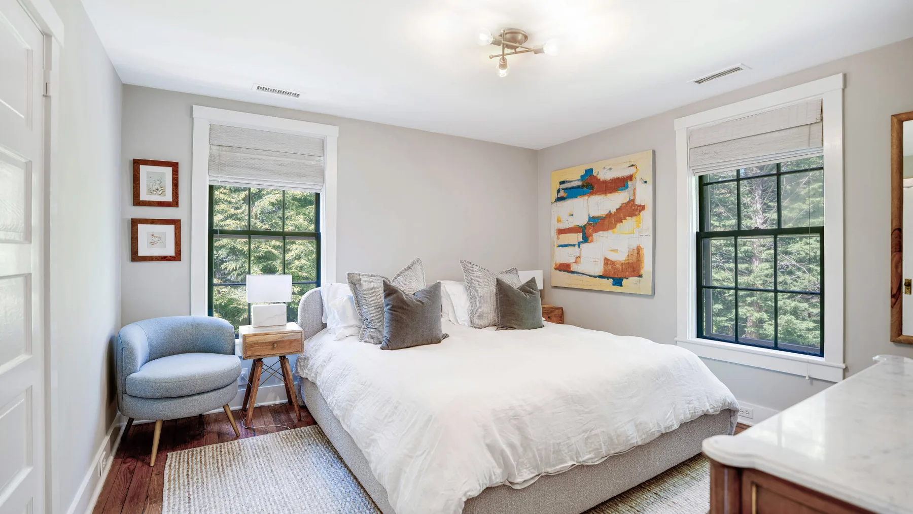 A bright bedroom with a large bed, two windows, and a cushioned seat.