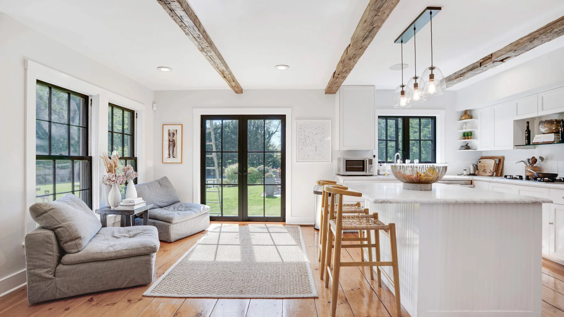 A bright open-plan living room and kitchen with large windows and a dining island.
