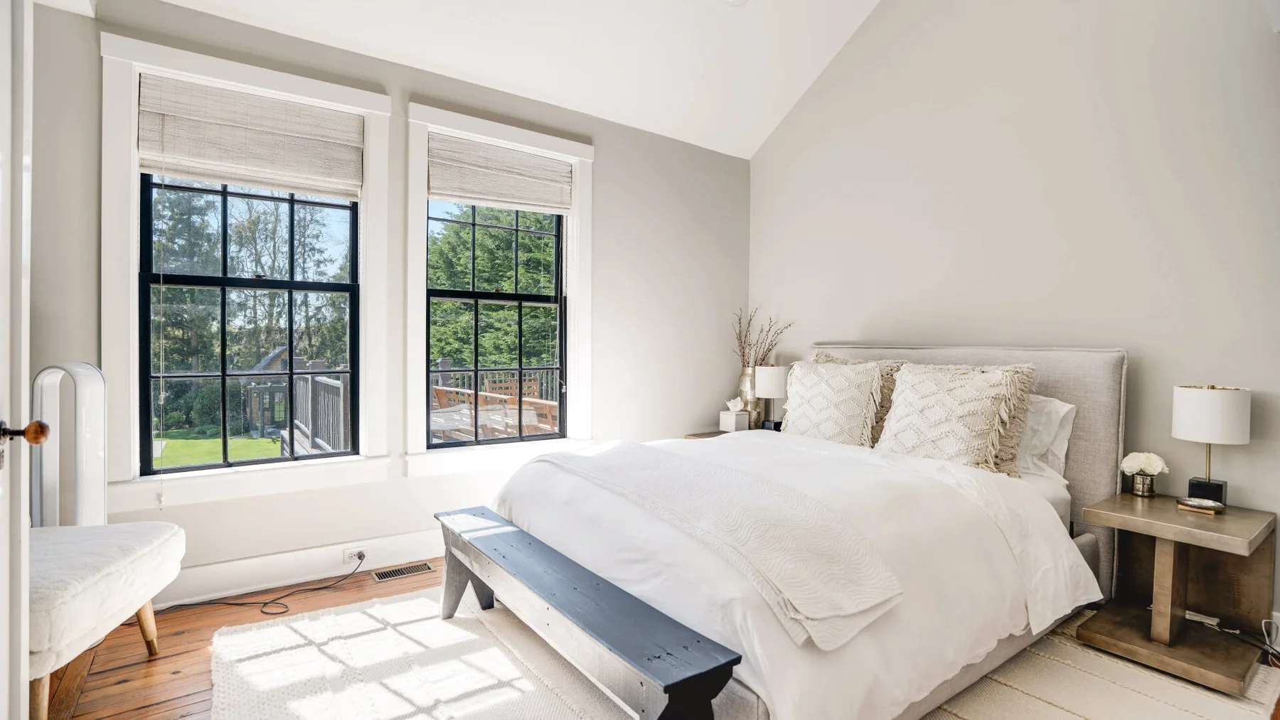 A bright bedroom with a neatly made bed beside two large windows.