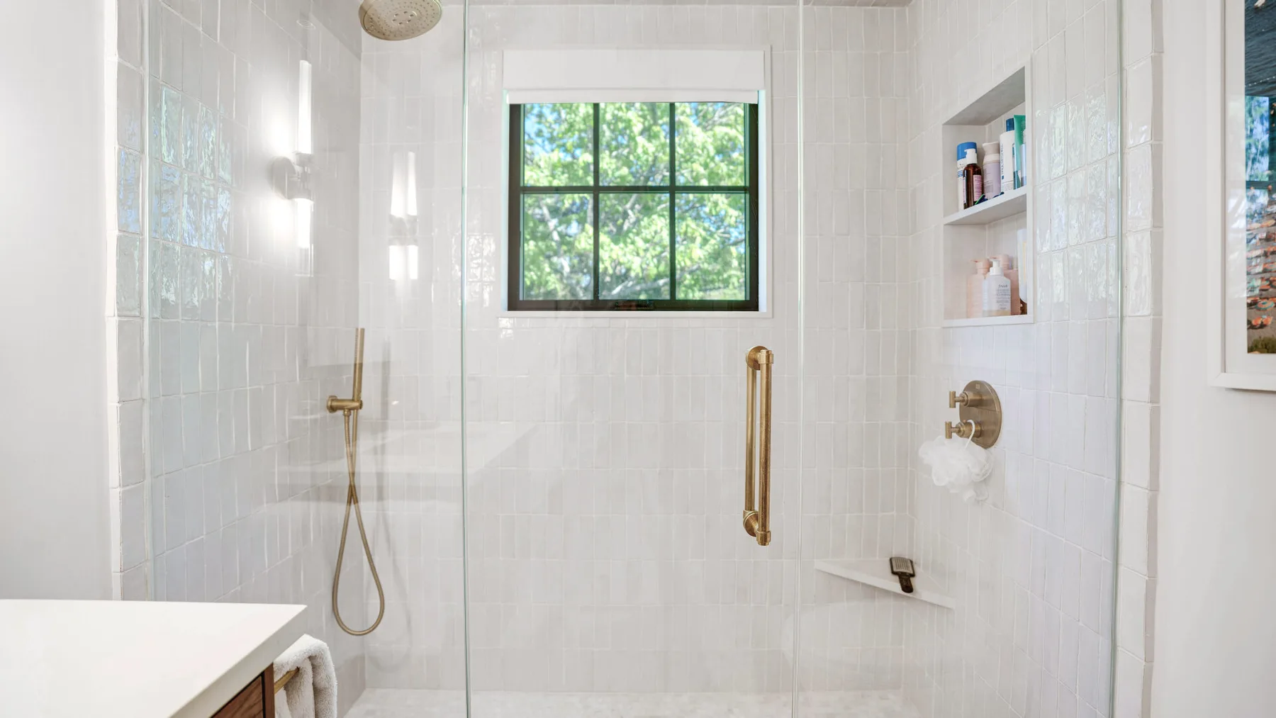 A bright tiled shower area has a window overlooking leafy trees.