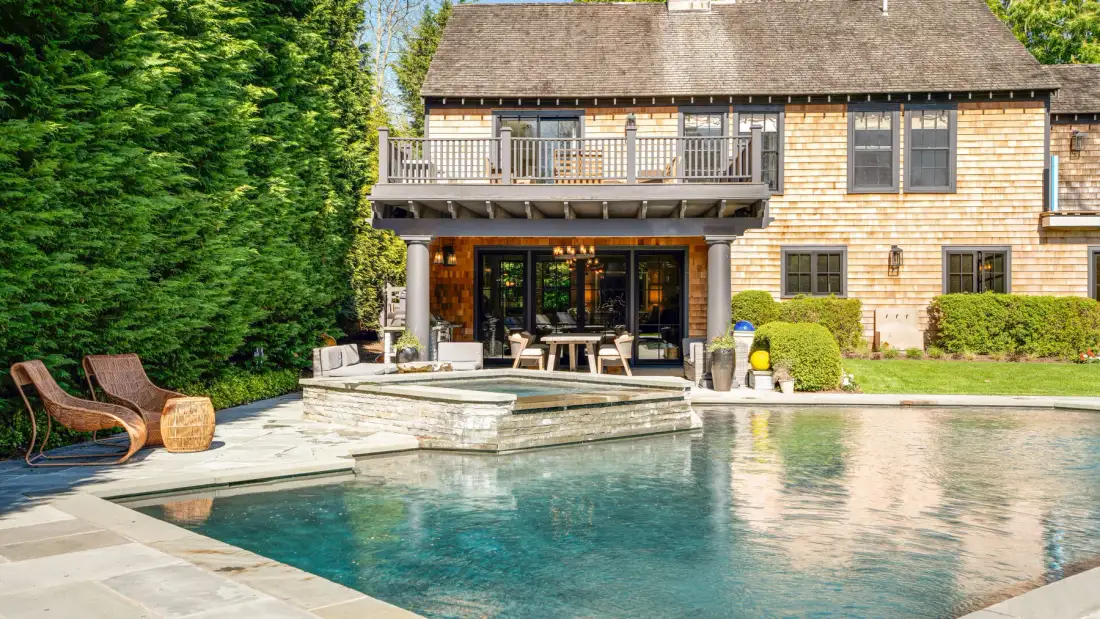 Una piscina junto a una casa, con un patio y asientos al aire libre.