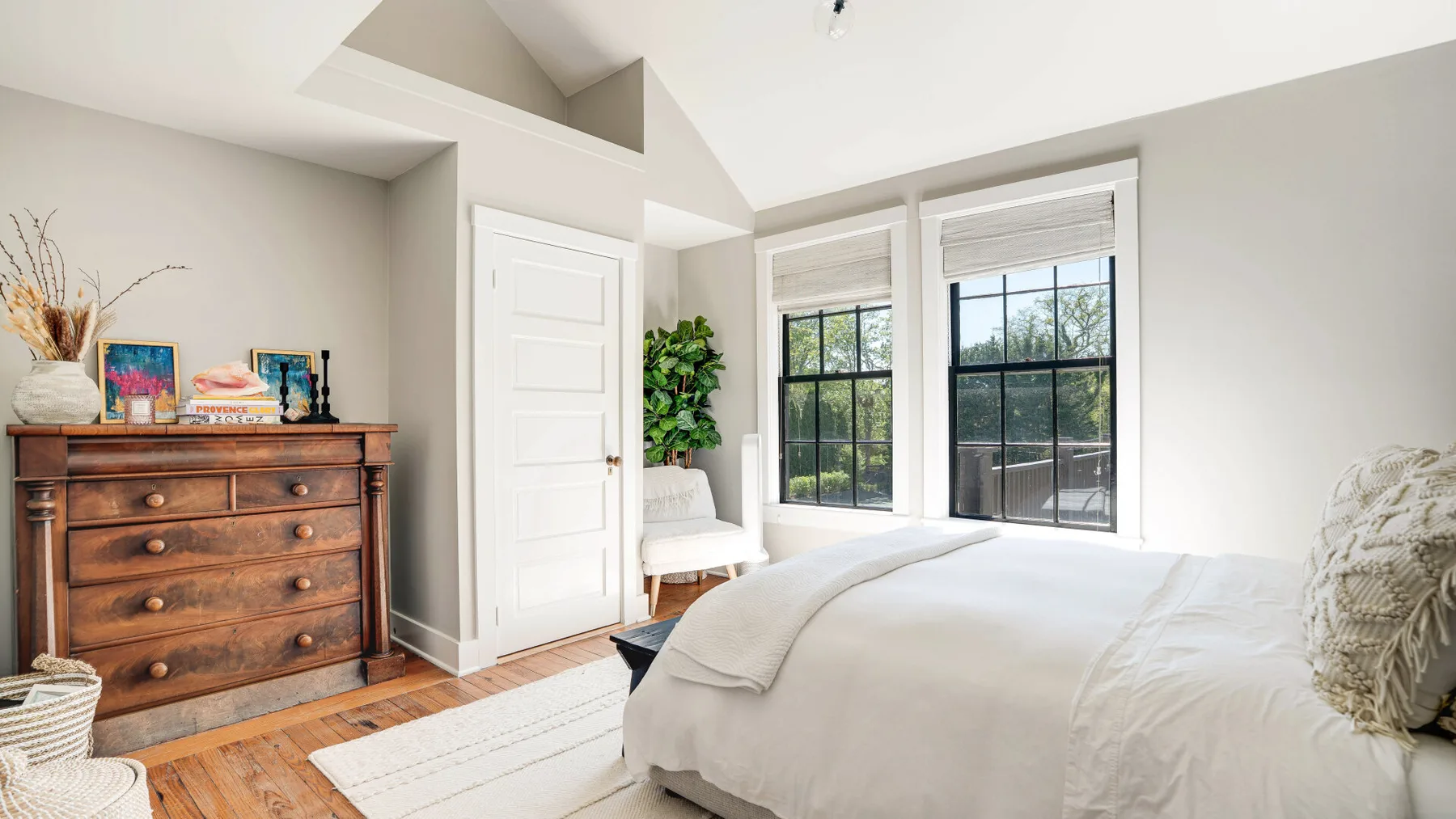 A bright bedroom with a white bed beside two large windows.