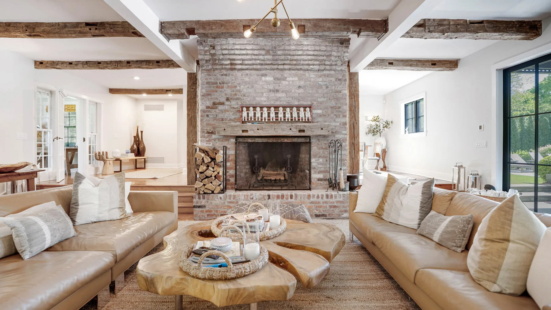 A bright living room with seating arranged around a prominent brick fireplace.