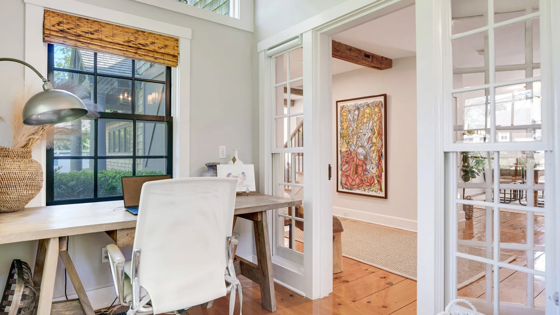 A bright home office with a desk and large windows beside a glass-paneled doorway.