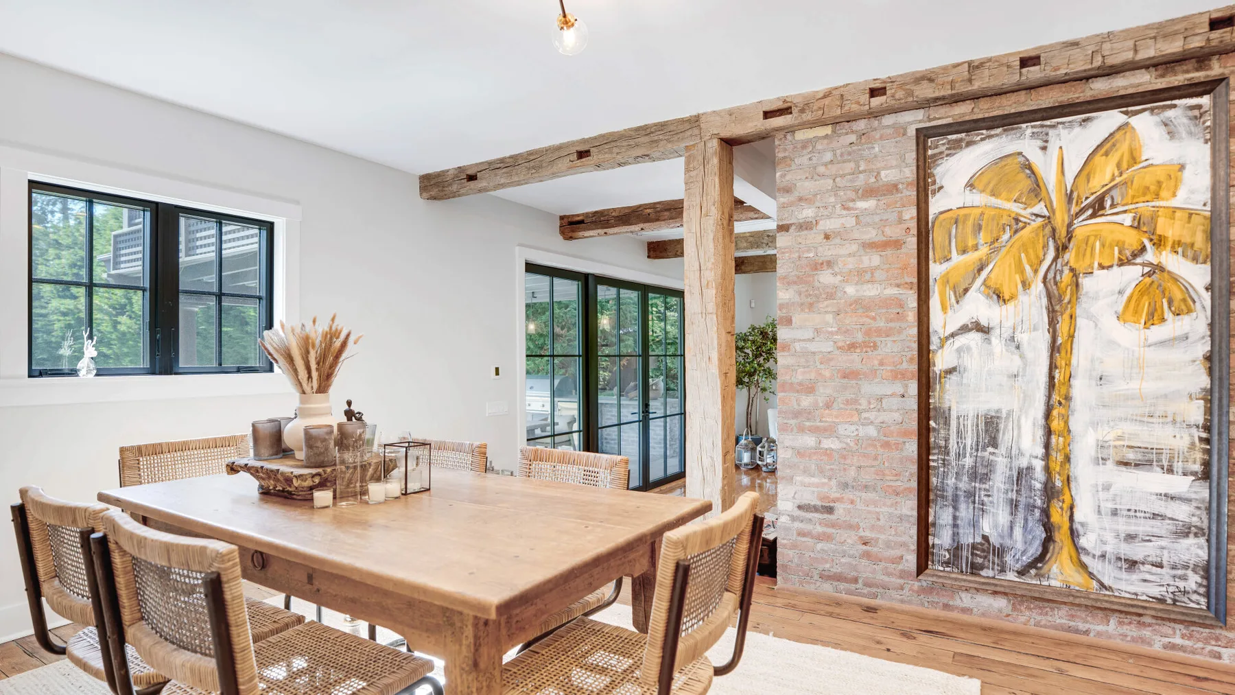 A dining area with a wooden table and chairs beside a brick wall and large artwork.