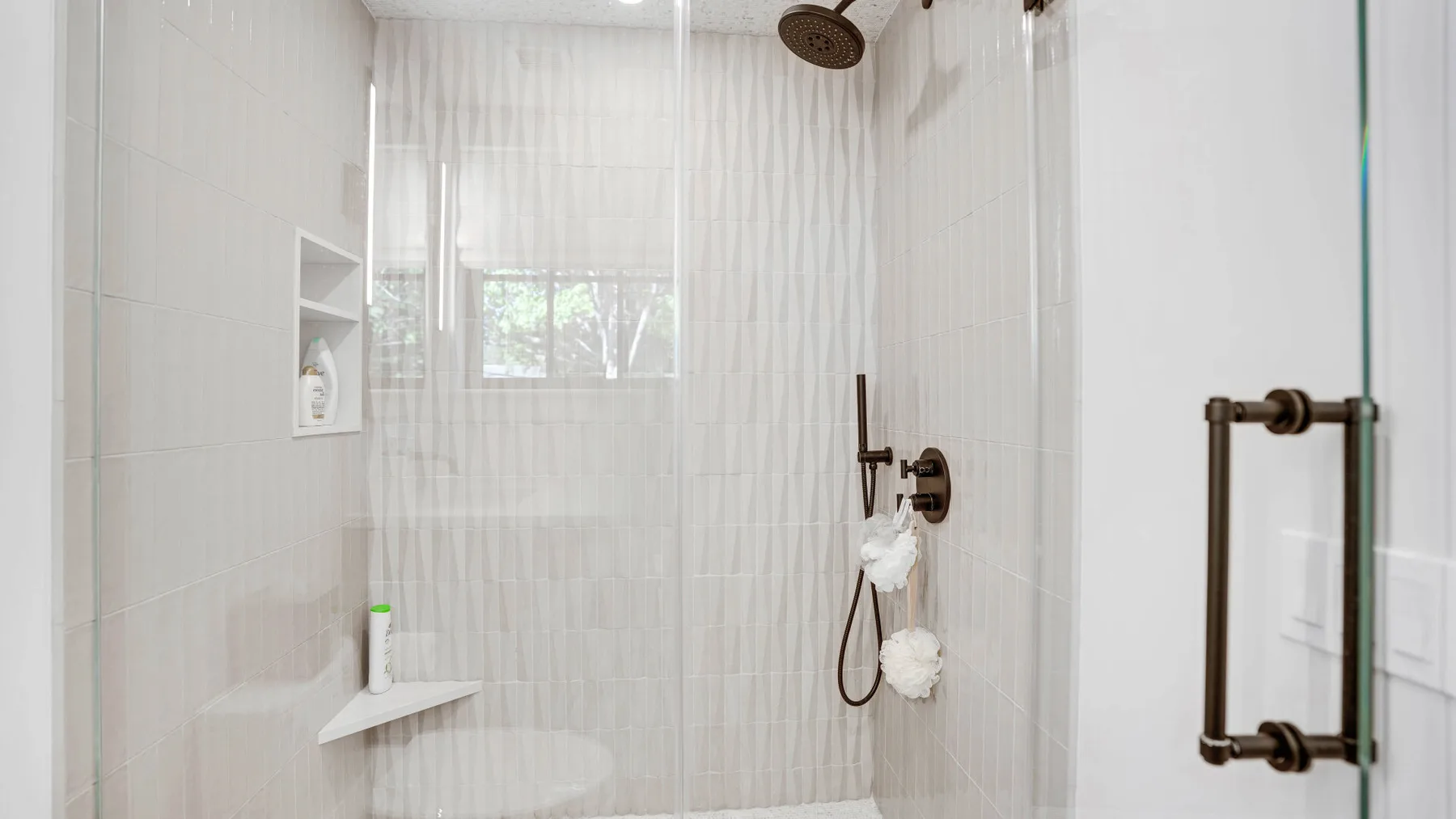 A tiled shower with built-in shelves and dark metal fixtures.