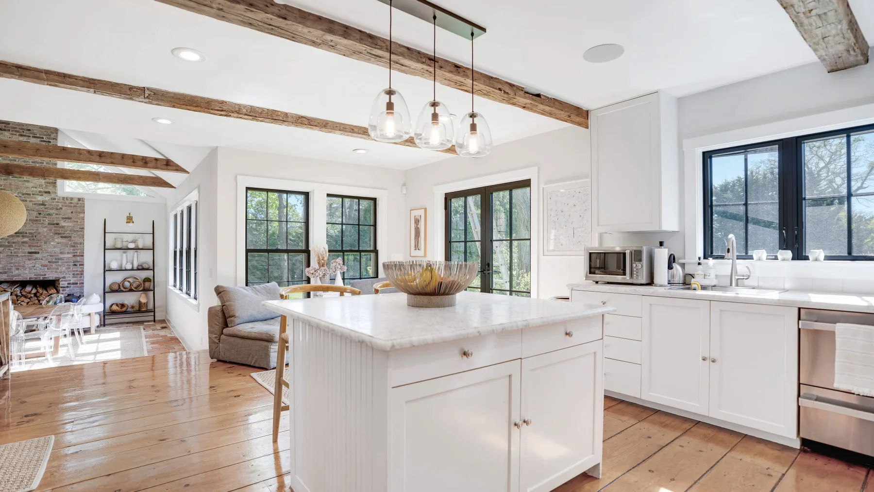 A bright kitchen with a large island, white cabinetry, and exposed wooden ceiling beams.