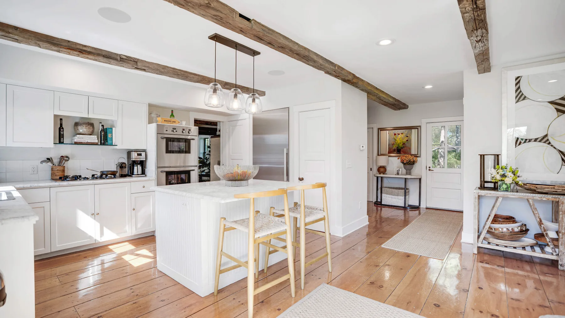 A bright kitchen with a white island and wooden beams overhead.