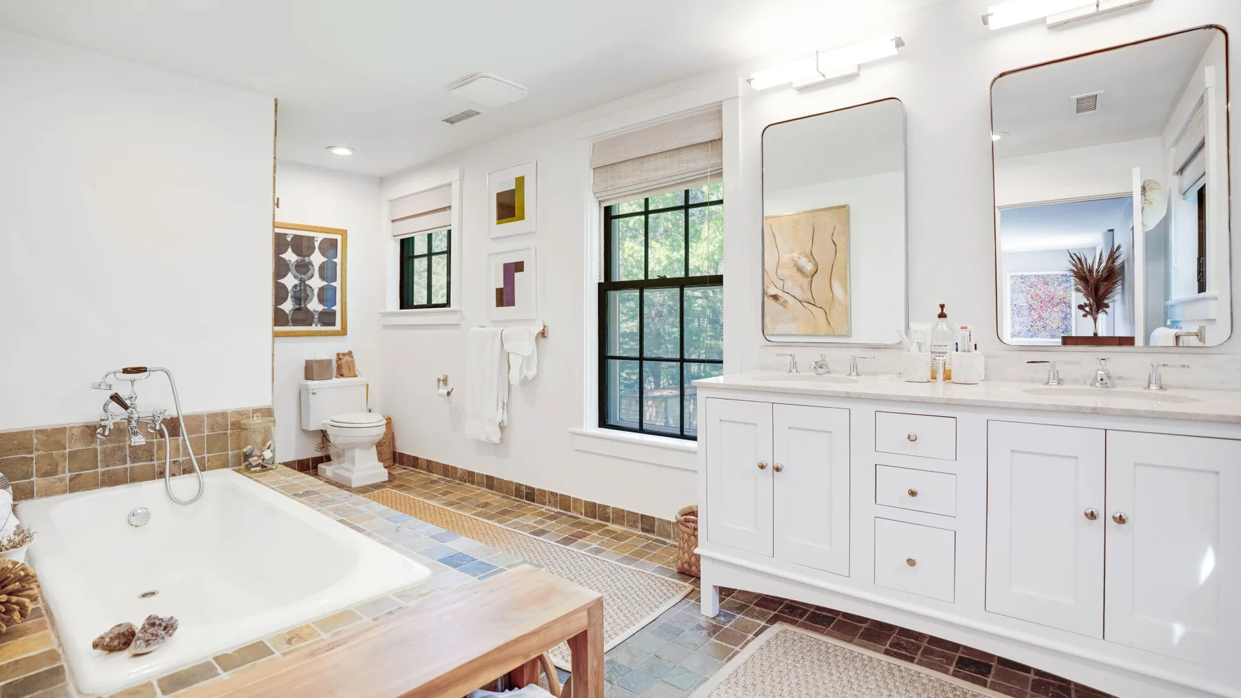 A bright bathroom with a bathtub, a window, and a long vanity.