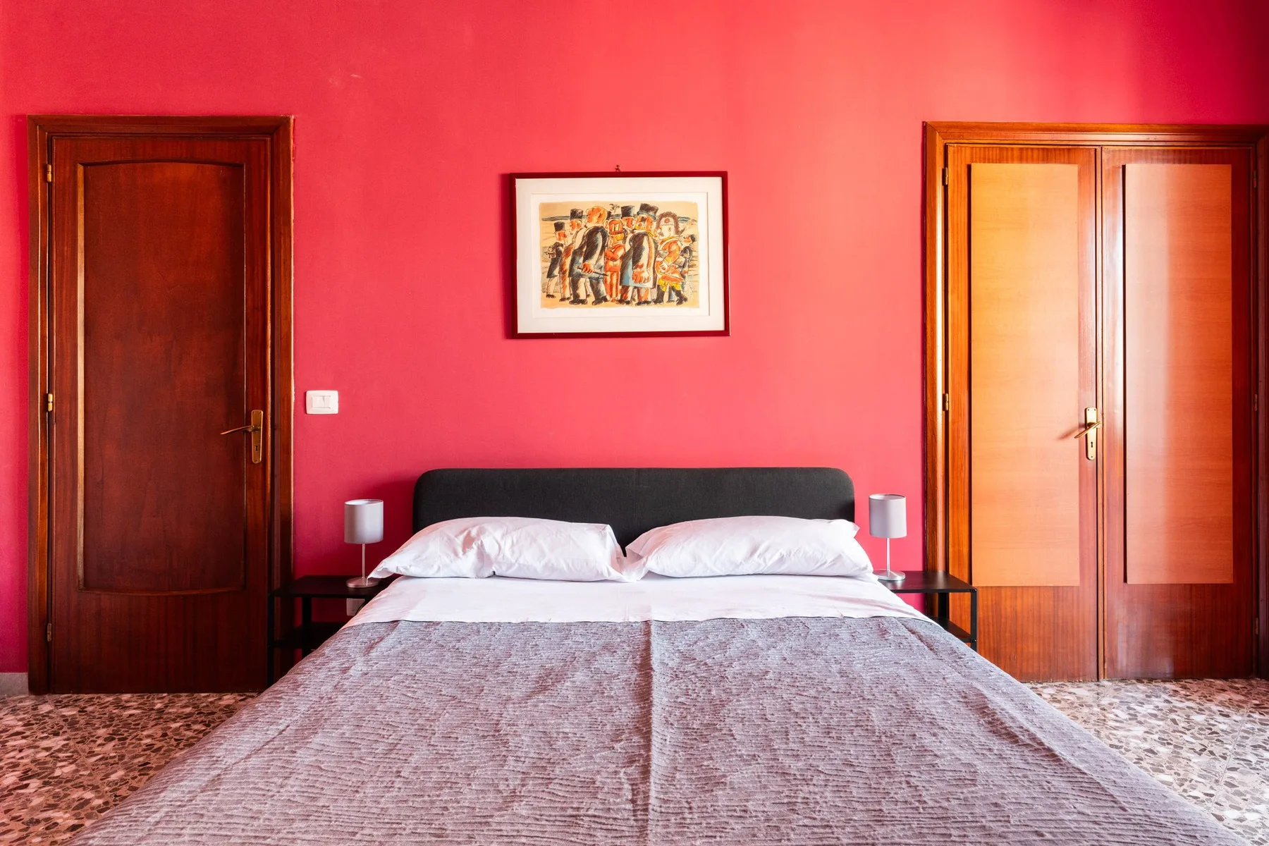 Un dormitorio con cama, mesitas de noche y una obra enmarcada sobre una pared rosa.