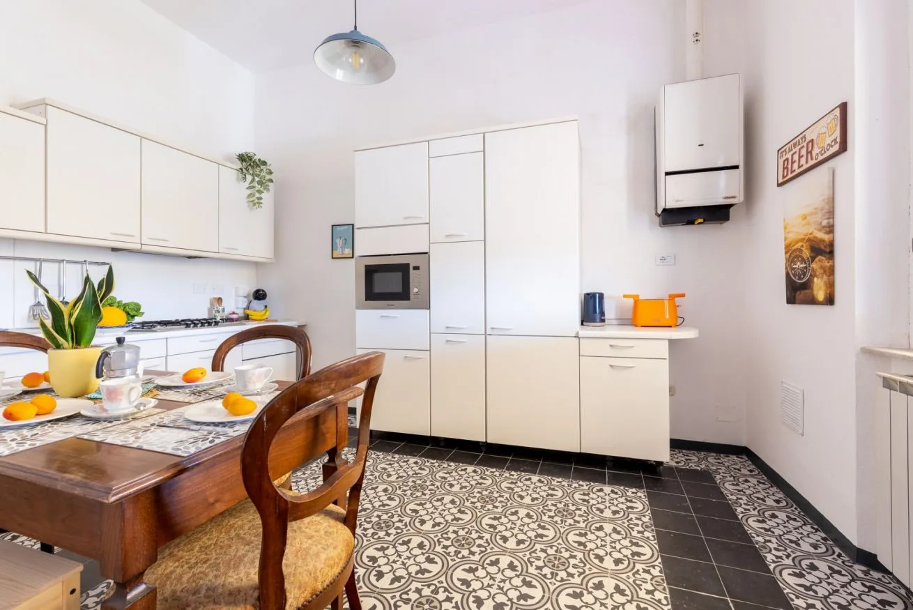 A bright kitchen with white cabinets, a dining table, and patterned floor tiles.