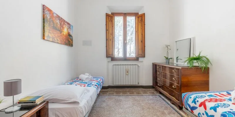 A bright bedroom with two beds, a wooden dresser, and a window.