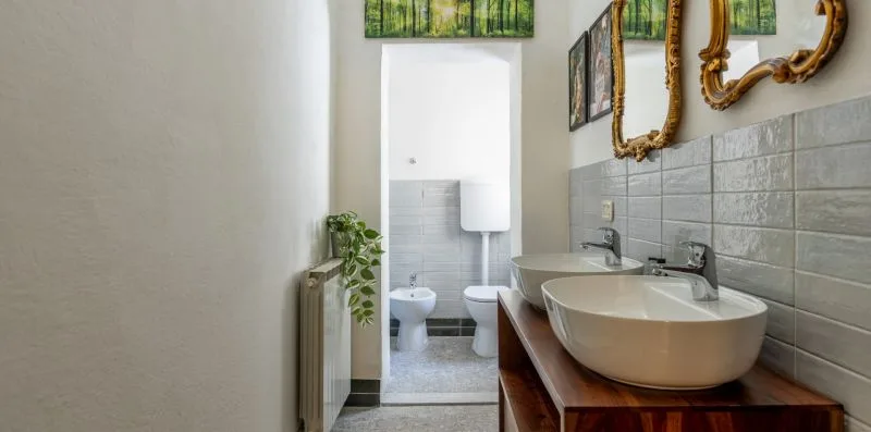 A bathroom with two vessel sinks and a toilet in the adjoining alcove.