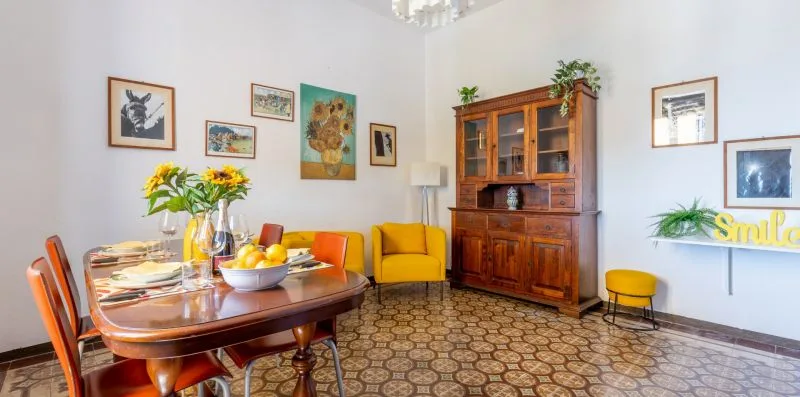 Un comedor y zona de estar con una mesa puesta, asientos amarillos y un armario de madera.