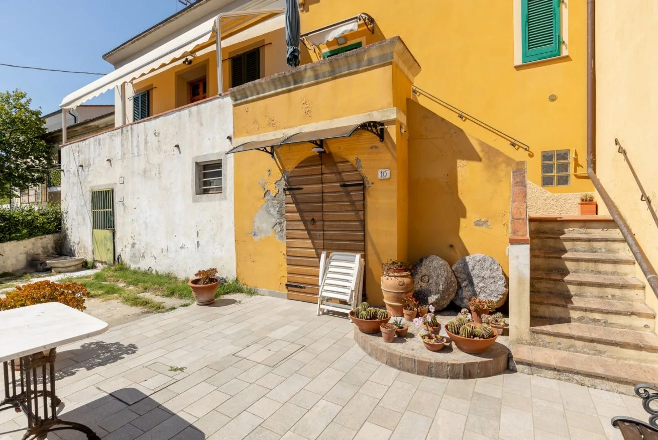 A yellow building opens onto a paved courtyard with potted plants and exterior stairs.