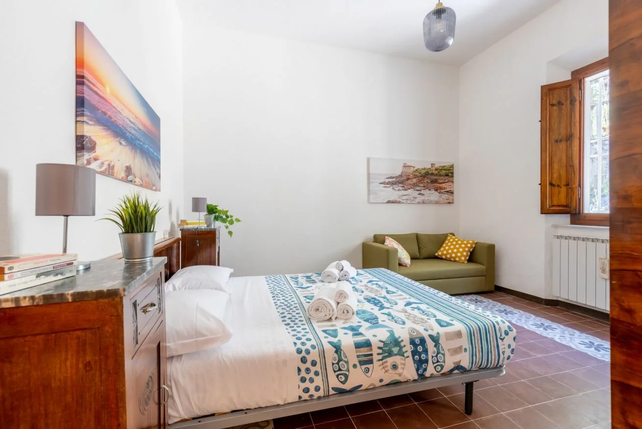 A bedroom with a bed, a small sofa, and a window.