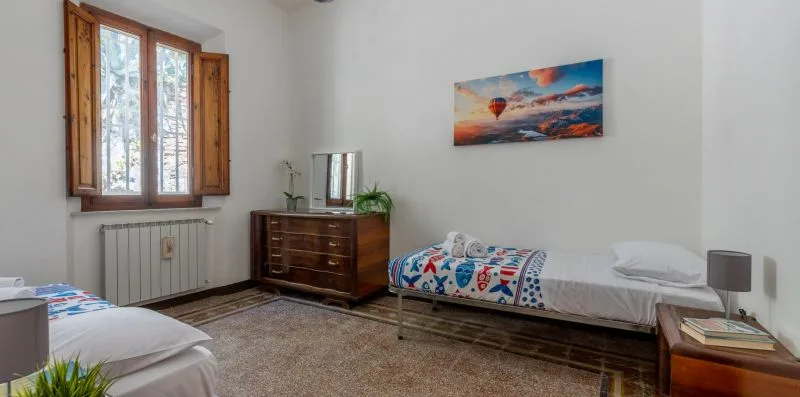 Un dormitorio luminoso con dos camas y una cómoda de madera bajo una ventana.