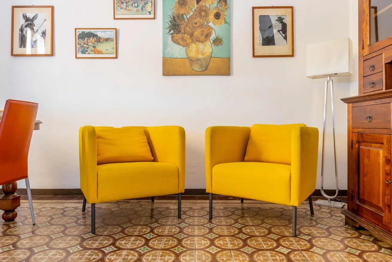 A living room with two yellow armchairs beneath framed artwork.