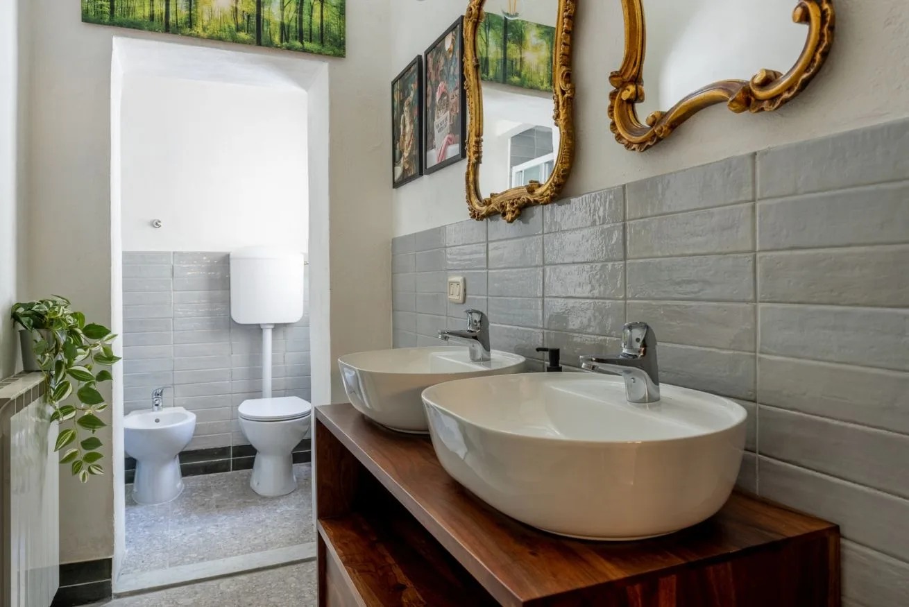 A bathroom vanity with two basin sinks sits beside a doorway to a tiled bathroom.