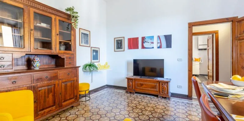 A furnished living room with wooden cabinets, a television, and patterned tile flooring.