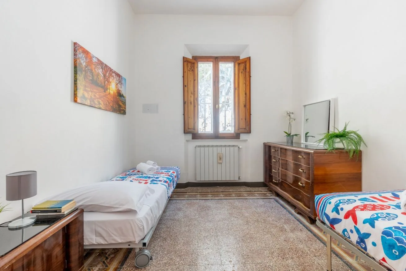 A bright bedroom with two beds, a window, and a wooden dresser.