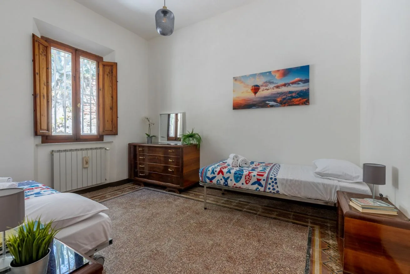 A bedroom with two beds, a window, and a colorful landscape picture.
