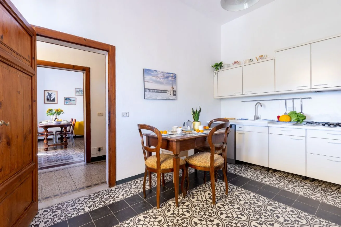 A dining area with a wooden table and chairs beside a white kitchen.
