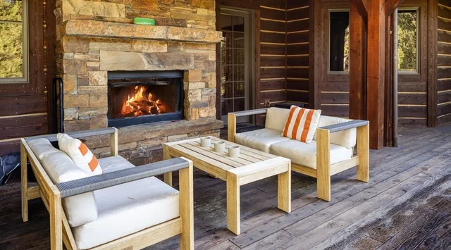 Una terraza de madera cubierta con asientos acolchados y una chimenea de piedra.