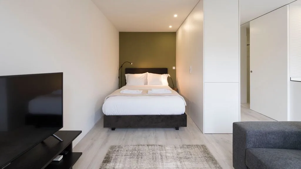 A bedroom with a bed, a television, and a gray seating area.