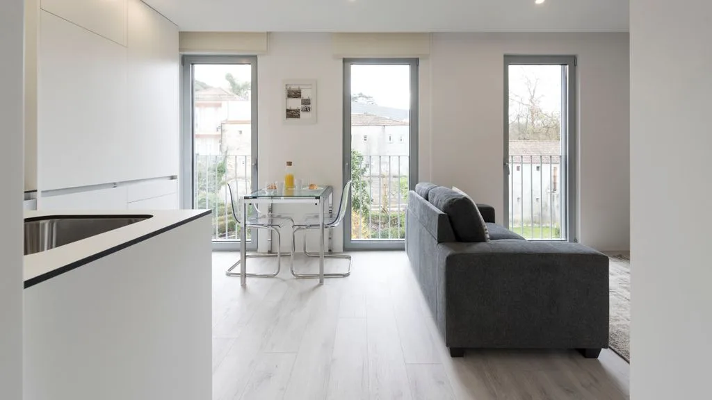 A bright open-plan living area with a gray sofa, dining table, and large windows.