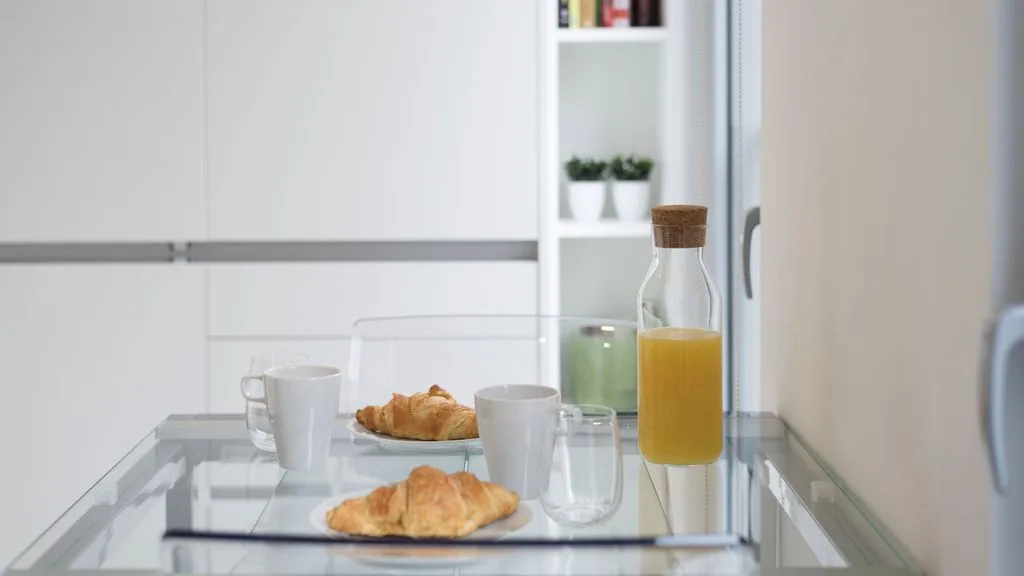 A bright kitchen counter displays pastries, cups, and a bottle of orange juice.
