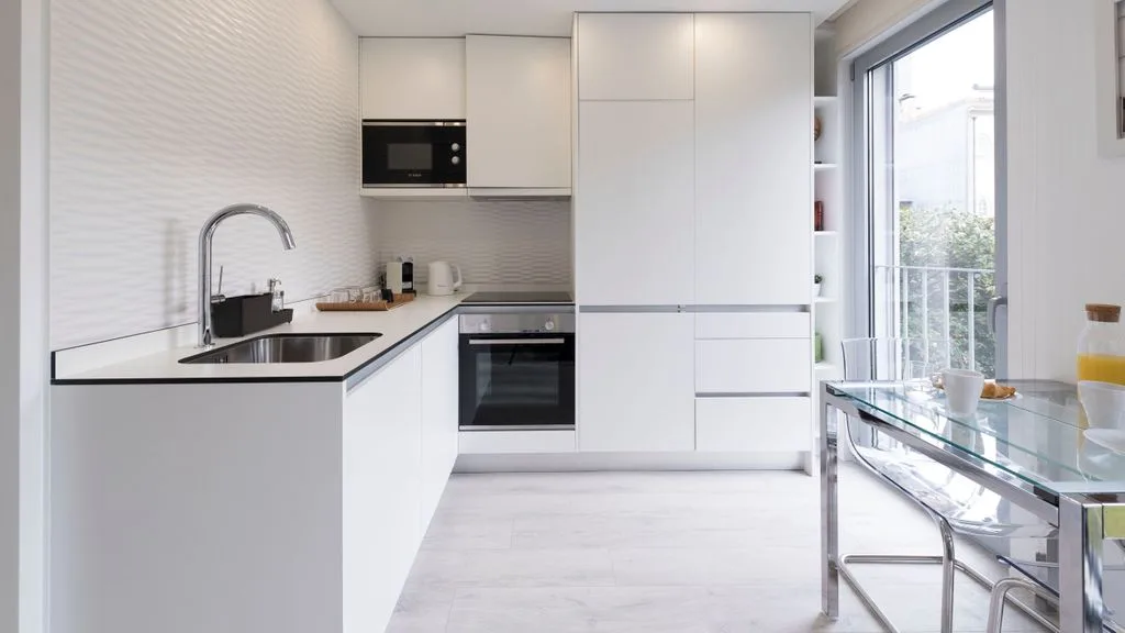 A bright modern kitchen with white cabinetry and a glass dining table.