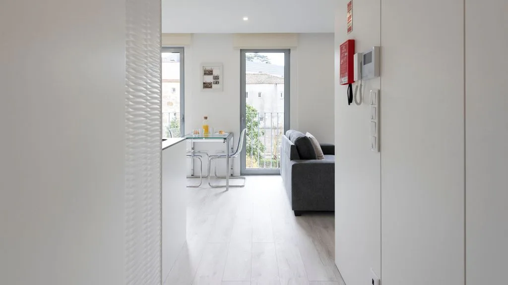 A bright living area opens onto a dining space beside tall windows.