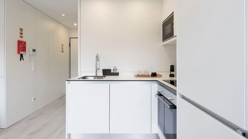 A bright modern kitchen with white cabinets, a sink, and built-in appliances.