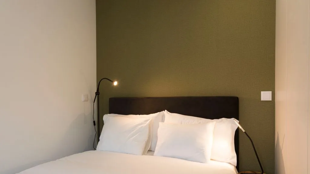 A bedroom with a bed, white bedding, and a bedside lamp.