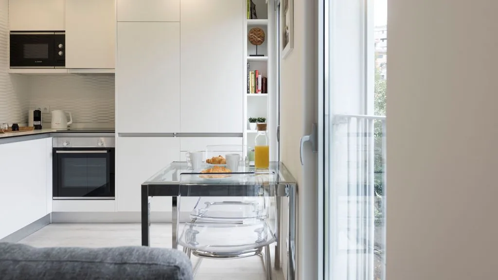 A bright kitchen and dining area with a glass table beside a large window.