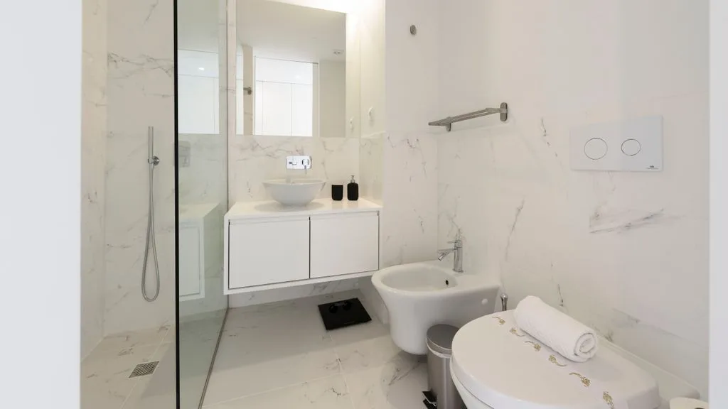 A bright bathroom with a glass shower, sink, and toilet.