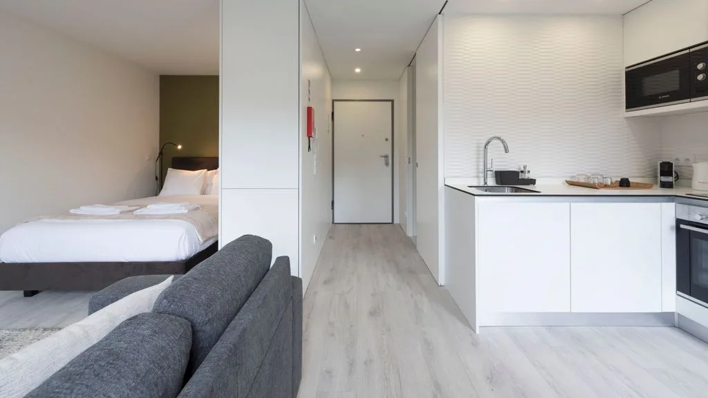 A compact open-plan room combines a sleeping area, seating, and a kitchen.