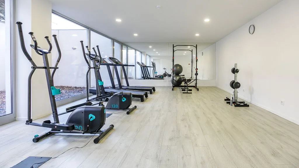 A bright gym with exercise machines arranged beside large windows.